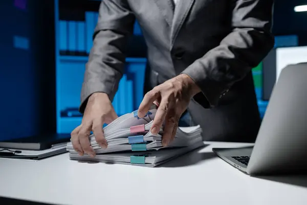 An employee held a large pile of documents in his hand, Large piles of work documents on desks are being sorted by employees, Important documents are stacked.