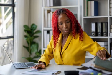 Şirketimizde özel bir ofiste oturan güzel bir Afrikalı iş kadını bir toplantıya hazırlanmak için bilgi arıyor masasında oturuyor ve farklı şeyler yapıyor..