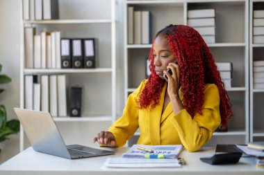 Güzel Afrikalı iş kadını iletişim kurmak ve bilgi bulmak için akıllı telefonu kullanıyor. Şu anda sorumlu olan işle ilgili olarak, bir kadın çalışan görevleri tamamlamak için bir iletişim cihazı kullanır..
