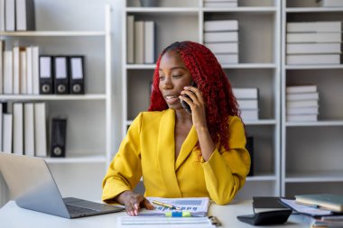 Güzel Afrikalı iş kadını iletişim kurmak ve bilgi bulmak için akıllı telefonu kullanıyor. Şu anda sorumlu olan işle ilgili olarak, bir kadın çalışan görevleri tamamlamak için bir iletişim cihazı kullanır..