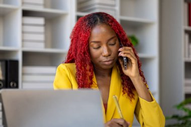 Güzel Afrikalı iş kadını iletişim kurmak ve bilgi bulmak için akıllı telefonu kullanıyor. Şu anda sorumlu olan işle ilgili olarak, bir kadın çalışan görevleri tamamlamak için bir iletişim cihazı kullanır..