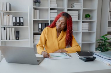 Şirketimizde özel bir ofiste oturan güzel bir Afrikalı iş kadını bir toplantıya hazırlanmak için bilgi arıyor masasında oturuyor ve farklı şeyler yapıyor..
