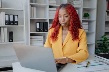 Şirketimizde özel bir ofiste oturan güzel bir Afrikalı iş kadını bir toplantıya hazırlanmak için bilgi arıyor masasında oturuyor ve farklı şeyler yapıyor..