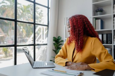 Şirketimizde özel bir ofiste oturan güzel bir Afrikalı iş kadını bir toplantıya hazırlanmak için bilgi arıyor masasında oturuyor ve farklı şeyler yapıyor..