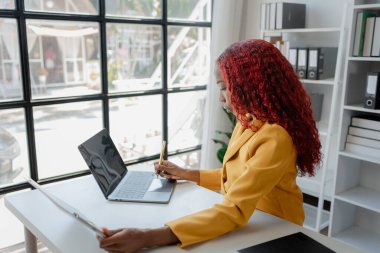 Şirketimizde özel bir ofiste oturan güzel bir Afrikalı iş kadını bir toplantıya hazırlanmak için bilgi arıyor masasında oturuyor ve farklı şeyler yapıyor..