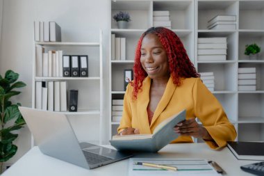 Şirketimizde özel bir ofiste oturan güzel bir Afrikalı iş kadını bir toplantıya hazırlanmak için bilgi arıyor masasında oturuyor ve farklı şeyler yapıyor..