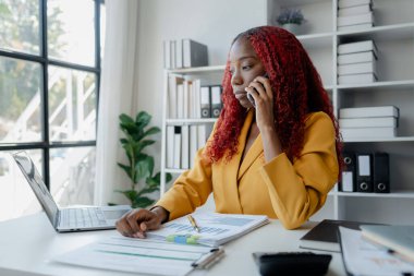 Güzel Afrikalı iş kadını iletişim kurmak ve bilgi bulmak için akıllı telefonu kullanıyor. Şu anda sorumlu olan işle ilgili olarak, bir kadın çalışan görevleri tamamlamak için bir iletişim cihazı kullanır..