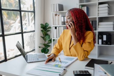 Güzel Afrikalı iş kadını iletişim kurmak ve bilgi bulmak için akıllı telefonu kullanıyor. Şu anda sorumlu olan işle ilgili olarak, bir kadın çalışan görevleri tamamlamak için bir iletişim cihazı kullanır..