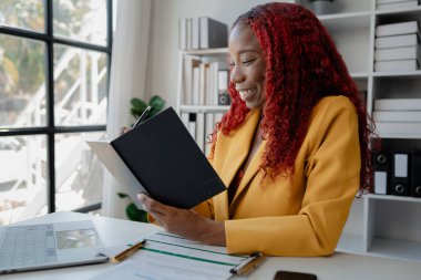 Şirketimizde özel bir ofiste oturan güzel bir Afrikalı iş kadını bir toplantıya hazırlanmak için bilgi arıyor masasında oturuyor ve farklı şeyler yapıyor..