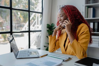 Güzel Afrikalı iş kadını iletişim kurmak ve bilgi bulmak için akıllı telefonu kullanıyor. Şu anda sorumlu olan işle ilgili olarak, bir kadın çalışan görevleri tamamlamak için bir iletişim cihazı kullanır..