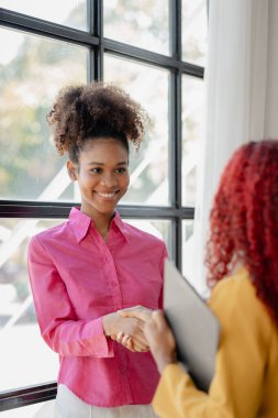 İki güzel Afrikalı kadın ofiste tokalaşırken önemli işler başarıyla tartışıldı. Güzel başarılı Afrikalı iş kadınları iş zaferi nedeniyle el ele tutuşuyorlar..