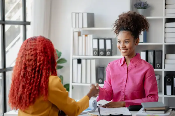 İki güzel Afrikalı kadın ofiste tokalaşırken önemli işler başarıyla tartışıldı. Güzel başarılı Afrikalı iş kadınları iş zaferi nedeniyle el ele tutuşuyorlar..