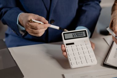 Meslektaşlar hesaplanmış sayıları inceler ve konferans odasında hangi sayının doğru olduğunu tartışırlar. Bir grup işadamı hesaplama ve sonuç alışverişi için bir hesap makinesi kullanır..