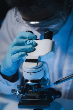 Bir bilim adamı mikrobiyoloji alanında mikroskop kullanarak örnekler üzerinde çalışıyor. Mikroskoplar kemoterapi araştırmaları için araştırmacılar tarafından kullanılıyor..