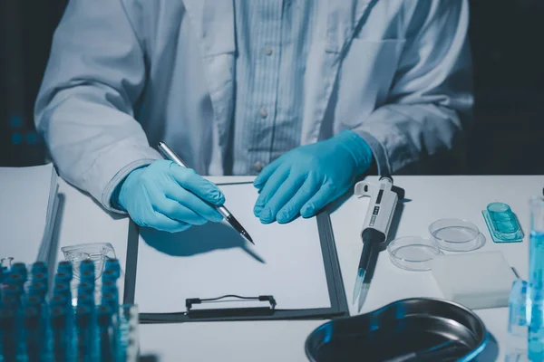 A scientist is writing down the results of an experiment in a report card, A laboratory full of scientific equipment for experiments, Many test tubes were analyzed by experts.