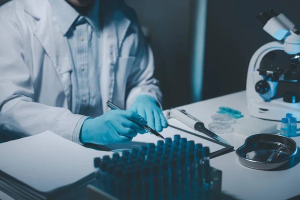 A scientist is writing down the results of an experiment in a report card, A laboratory full of scientific equipment for experiments, Many test tubes were analyzed by experts.