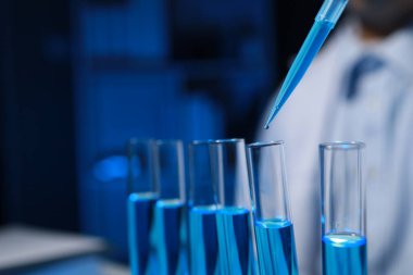 Bir kimyager, laboratuvarında çeşitli bilimsel ekipmanlar kullanarak yeni keşfedilen bir kimyasalı test ediyor..