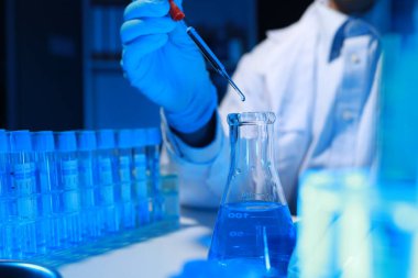 Bir kimyager, laboratuvarında çeşitli bilimsel ekipmanlar kullanarak yeni keşfedilen bir kimyasalı test ediyor..