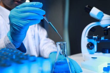 Bir kimyager, laboratuvarında çeşitli bilimsel ekipmanlar kullanarak yeni keşfedilen bir kimyasalı test ediyor..