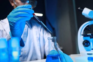 Bir kimyager, laboratuvarında çeşitli bilimsel ekipmanlar kullanarak yeni keşfedilen bir kimyasalı test ediyor..