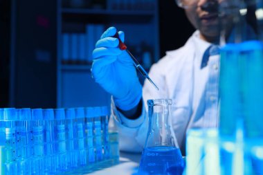 Bir kimyager, laboratuvarında çeşitli bilimsel ekipmanlar kullanarak yeni keşfedilen bir kimyasalı test ediyor..