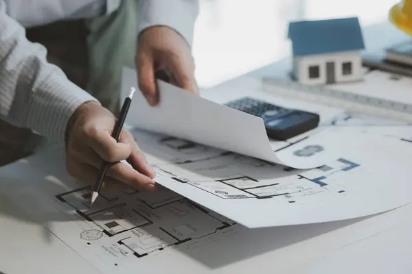 An engineer is studying blueprints to better understand the work to be done, An architect looks at building plans in his private office to understand the work assigned to him by his boss.