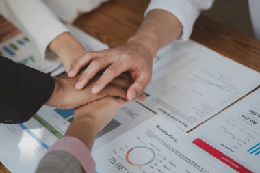 Bir grup çalışan, şirketin önemli bir müşterisi tarafından verilen büyük bir projeye başlamadan önce el ele tutuşup el ele tutuşarak birbirlerine yardım etme jestinde bulunuyor..