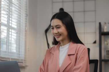 Güzel genç bir Asyalı kadın özel bir ofiste mutlu bir şekilde oturuyor. Yüzlerinde tebessümle odada oturan kadın çalışanların olduğu özel bir ofisteki atmosfer..