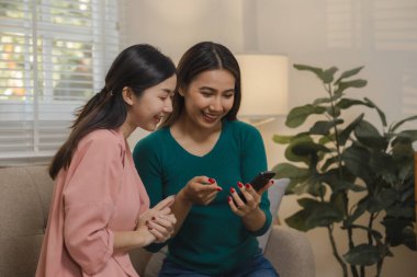 İki güzel Asyalı kadın kendilerini dairelerinde grup aktivitesi olarak eğlendirmek için elektronik cihazlar kullanıyorlar hafta sonları evlerindeki kanepede birlikte vakit geçiriyorlar..