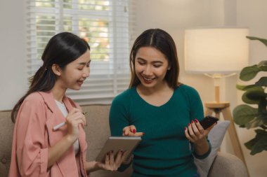 İki güzel Asyalı kadın kendilerini dairelerinde grup aktivitesi olarak eğlendirmek için elektronik cihazlar kullanıyorlar hafta sonları evlerindeki kanepede birlikte vakit geçiriyorlar..