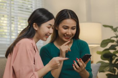 İki güzel Asyalı kadın kendilerini dairelerinde grup aktivitesi olarak eğlendirmek için elektronik cihazlar kullanıyorlar hafta sonları evlerindeki kanepede birlikte vakit geçiriyorlar..