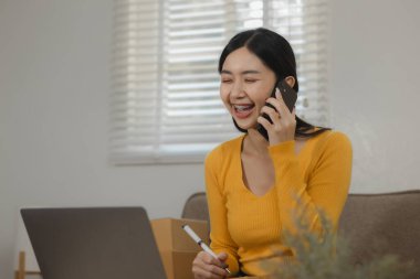 Çevrimiçi küçük bir işletmenin güzel bir kadın girişimcisi kişisel deposunda içi mal dolu kutularla gururla çalışıyor, ürünü teslim etmeden önce müşteri bilgilerini kontrol ediyor.