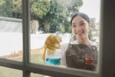 Penceredeki camları temizlemek için havlu kullanıyor ve ellerini korumak için eldiven giyiyor. Ev işi yaparken önlük takıyor, pencereye sıkarak temizliyor.