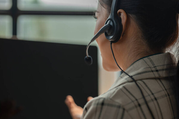 Азиатская женщина работает в качестве службы поддержки колл-центра, этот сотрудник, как телемаркетинг дает советы клиенту, она носит гарнитуру, чтобы поговорить с клиентом и помочь им через телефон доверия