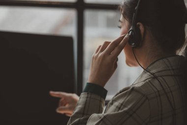 Asyalı bir kadın çağrı merkezi desteği olarak çalışıyor, bu çalışan müşteriye bir tavsiyede bulunuyor, müşteriyle konuşmak ve onlara yardım etmek için kulaklık takıyor.