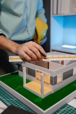 bir mimar ev modeli yenileme üzerinde çalışıyor, bir mühendis işyerinde çalışıyor, kaskı tutuyor, ev modeli mimarlar tarafından yapıyı daha istikrarlı hale getirmek için modifiye edildi.