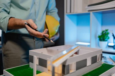 bir mimar ev modeli yenileme üzerinde çalışıyor, bir mühendis işyerinde çalışıyor, kaskı tutuyor, ev modeli mimarlar tarafından yapıyı daha istikrarlı hale getirmek için modifiye edildi.