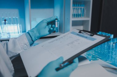 Bir bilimadamı laboratuarda çalışıyor ve deney sonuçlarını not alıyor. Evrakların üzerinde kimyasal bir isim var. Araştırmadan sonra tüm örnekleri alıp sonuç almak için bir kimyagerin bunları kağıt raporuna yazması gerekiyor.