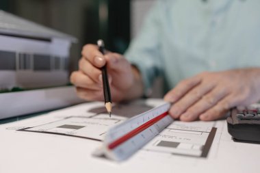 Mimar, yaratıcılığını, tasarılarını kullanarak ve mimarın masasında tasarım evraklarıyla dolu inşaat tasarım ekipmanları kullanarak önemli bir projenin taslağı üzerinde çalışıyor.