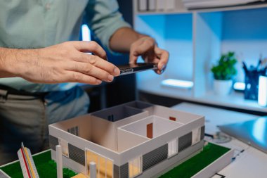 Mühendis ofiste büyük bir proje yapıyor, bir mimar işini kolaylaştırmak için elektronik cihaz kullanıyor, plan ve model masanın üzerinde, çalışan konsantrasyonla çalışıyor.
