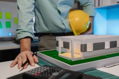 bir mimar ev modeli yenileme üzerinde çalışıyor, bir mühendis işyerinde çalışıyor, kaskı tutuyor, ev modeli mimarlar tarafından yapıyı daha istikrarlı hale getirmek için modifiye edildi.