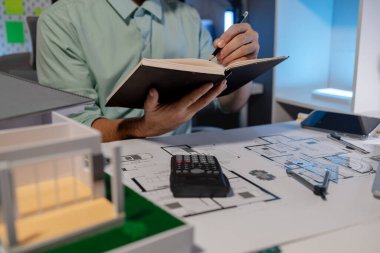 Mimar, yaratıcılığını, tasarılarını kullanarak ve mimarın masasında tasarım evraklarıyla dolu inşaat tasarım ekipmanları kullanarak önemli bir projenin taslağı üzerinde çalışıyor.