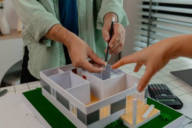 Bir mimar ve mühendis takım olarak çalışır, bir mühendis iş arkadaşıyla ev modelinin detaylarını tartışır. Aynı olduğundan emin olmak için planlarla karşılaştırır.