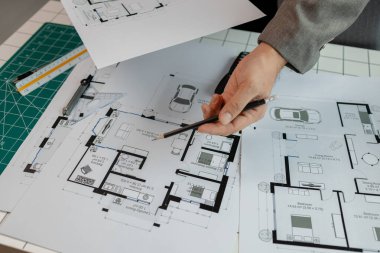 Ofiste bir mimar çalışıyor. Masanın üzerinde planlar ve ev modelleri var. Mühendis son bir kez daha mevcut olacak işleri kolaylaştırmak için araç kullanıyor.