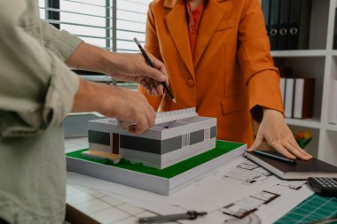 Bir mimar ve mühendis takım olarak çalışır, bir mühendis iş arkadaşıyla ev modelinin detaylarını tartışır. Aynı olduğundan emin olmak için planlarla karşılaştırır.