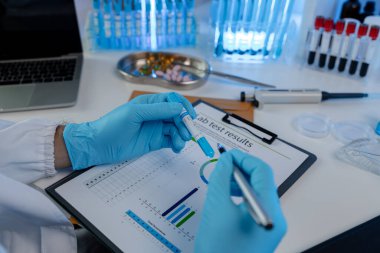 Bir bilim adamı kimyasal testlere katılan araştırmacılardan alınan laboratuvar sonuçlarını ve belgeleri inceliyor, kimyager test sonuçları belgelerini okumaya odaklanıyor