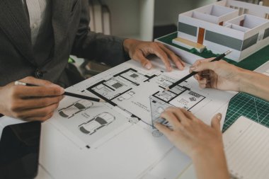 Mühendisler oturmuş yapıyı güçlendirmek için gözden geçirilmesi gereken bir inşaat planını tartışıyorlar. Bir mimar ve asistan planları inceliyor ve inceliyor.