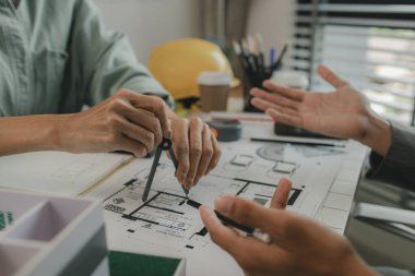 Mühendisler oturmuş yapıyı güçlendirmek için gözden geçirilmesi gereken bir inşaat planını tartışıyorlar. Bir mimar ve asistan planları inceliyor ve inceliyor.