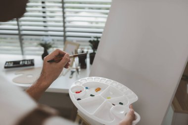 Bir sanatçı kendi resim stüdyosunda tuval, palet, suluboya, yağlar, poster renkleri, sanatsal, ressam, renkler, yaratıcılık, beceri gibi çeşitli resim aletleriyle oturuyor.