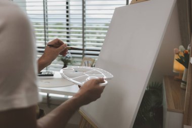 Bir sanatçı kendi resim stüdyosunda tuval, palet, suluboya, yağlar, poster renkleri, sanatsal, ressam, renkler, yaratıcılık, beceri gibi çeşitli resim aletleriyle oturuyor.